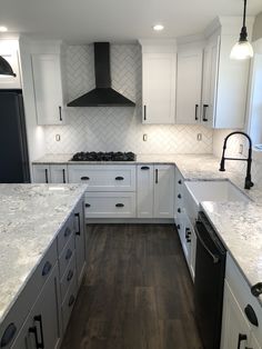 a large kitchen with white cabinets and marble counter tops, an oven hood over the range