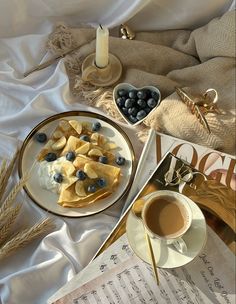 a plate with blueberries, bananas and cream on it next to a cup of coffee