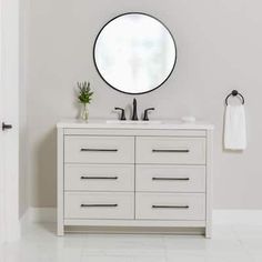 a white bathroom with a round mirror above the sink