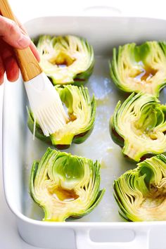 someone using a brush to clean the artichokes in a baking dish with oil