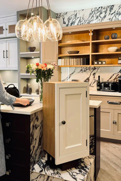 a woman standing in a kitchen next to a counter top with a cabinet on it