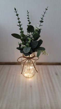 a mason jar filled with greenery and lights on top of a wooden table next to a wall