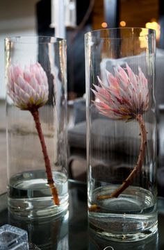 two vases with flowers in them sitting on a glass table next to each other