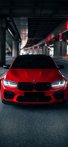 a red car is parked in an underground parking garage with its lights on and it's hood up