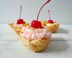 three small cupcakes with cherries and whipped cream on them are sitting on a white surface