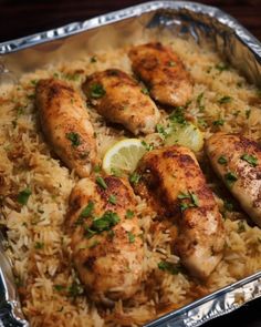 some chicken and rice in a pan with lemon wedges on the side for garnish