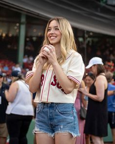 a woman standing in front of a crowd with her hands clasped to her chest and looking at the camera