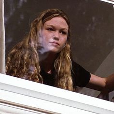 a woman is looking out the window with her hair blowing in the wind and holding a cell phone to her ear