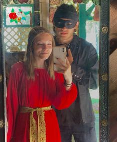 a woman in a red dress taking a selfie with a man wearing a mask