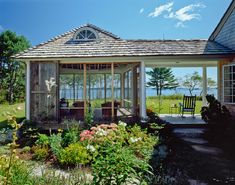 a gazebo in the middle of a garden with flowers and plants around it, next to a body of water