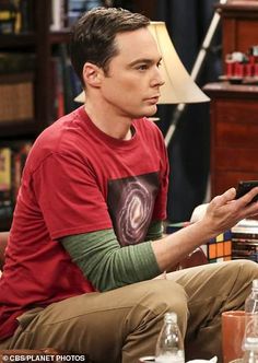 the young man is looking at his cell phone while sitting in front of a book shelf