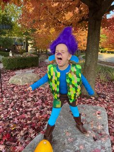 a young child dressed as a clown standing on a rock in the fall with his mouth open