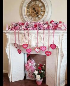 a decorated fireplace with pink and red hearts hanging from it's mantel, next to a potted plant