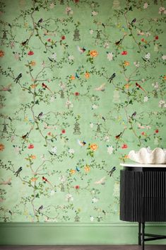 a green wallpaper with birds and flowers on it, next to a black cabinet