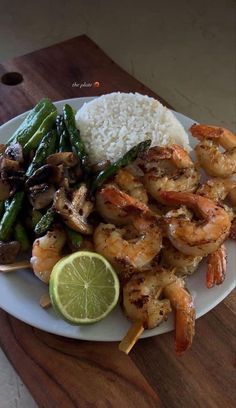 a plate with shrimp, rice and asparagus next to a slice of lime