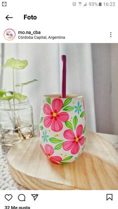 a pink flowered cup sitting on top of a wooden table next to a plant