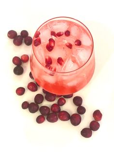 a glass filled with ice and cranberries on top of a white table next to it