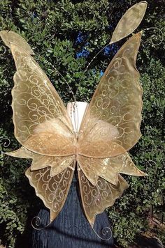 a metal butterfly sculpture sitting on top of a wooden post in front of some trees