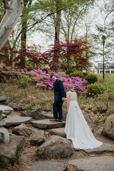 a bride and groom are standing on some rocks in front of pink flowers at their wedding