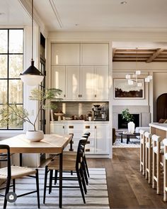 a dining room table and chairs in front of a kitchen with white cabinets, wood floors and an open fireplace