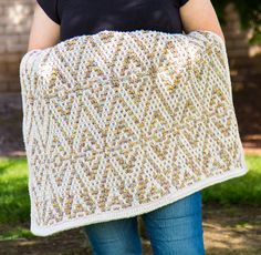 a woman is holding up a crocheted blanket