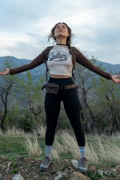 Woman stands with arms outstretched, eyes closed, enjoying the peace of a mountainous landscape at dusk. Hipster Camping Outfit, Legging Hiking Outfit, Feminine Camping Outfit, Camping Trip Outfits, Fuge Camp, Cold Hiking Outfit, Camping Aesthetic Outfits, Outdoor Camping Outfits, Traveler Outfit