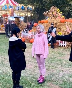 two people dressed in costumes are standing on the grass near an amusement park with pumpkins