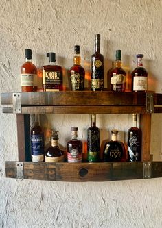 a wooden shelf filled with different types of liquors on top of a white wall