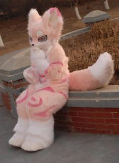 a white and pink stuffed animal sitting on top of a brick wall next to a pile of hay