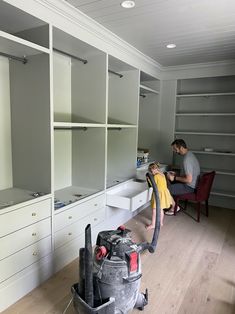 a man is cleaning the floor with a vacuum cleaner and another person sits in the background