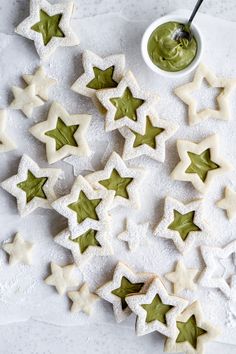 cookies with green icing and stars are arranged on a white surface next to a bowl of dip