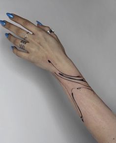 a woman's hand with blue fingernails and tattoos on her left arm, holding onto the wrist