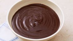 a white bowl filled with chocolate sauce on top of a blue and white towel next to a cup