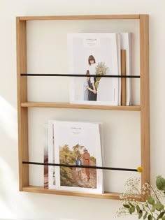 two wooden shelves with pictures and black wire on the top one shelf is holding magazines