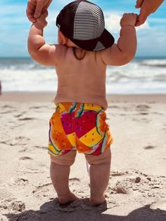 a small child standing on top of a beach next to an adult holding his hand