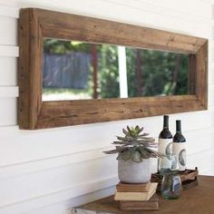 a wooden mirror hanging on the side of a wall next to a plant and bottles