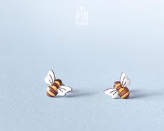 two small bee shaped earrings sitting on top of each other in front of a blue background