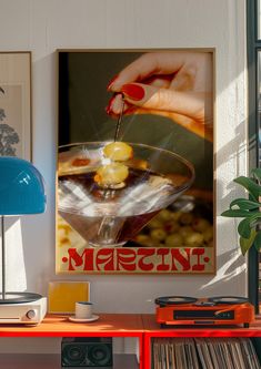 a woman's hand holding a martini glass in front of a poster on the wall