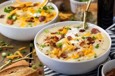 two bowls of potato soup with bacon, cheese and green onions on a wooden table