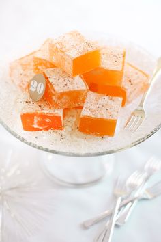 small pieces of orange and white cake on a glass plate with utensils next to it