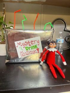 an elf is sitting on a desk with a sign that says, mystery drink challenge