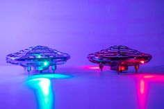 two flying saucers with colored lights on the bottom and one in the middle, sitting next to each other