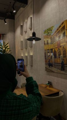 a person in a green hoodie taking a photo with their cell phone while sitting at a table