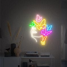 a neon sign with butterflies on it next to a white shelf and vase filled with flowers