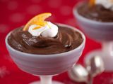 two glasses filled with chocolate pudding and topped with an orange peel on the top one