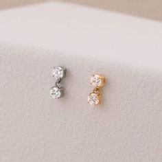 three pairs of diamond stud earrings sitting on top of a white surface in front of a wall