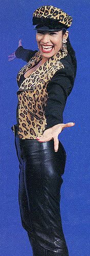 a woman wearing a leopard print top and black leather pants with her arms in the air