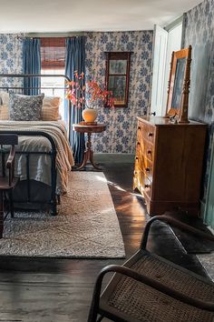 a bedroom with blue floral wallpaper and wooden furniture