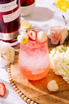 a pink drink with strawberries in it on a wooden platter next to flowers