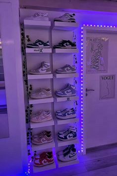 there are many pairs of shoes on the shelves in front of the door that is lit up with purple lights